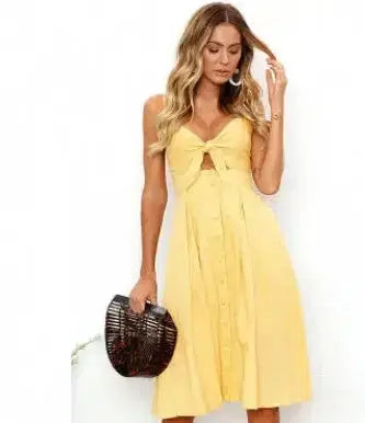 Yellow sleeveless midi dress with front knot detail and button closure, paired with woven handbag
